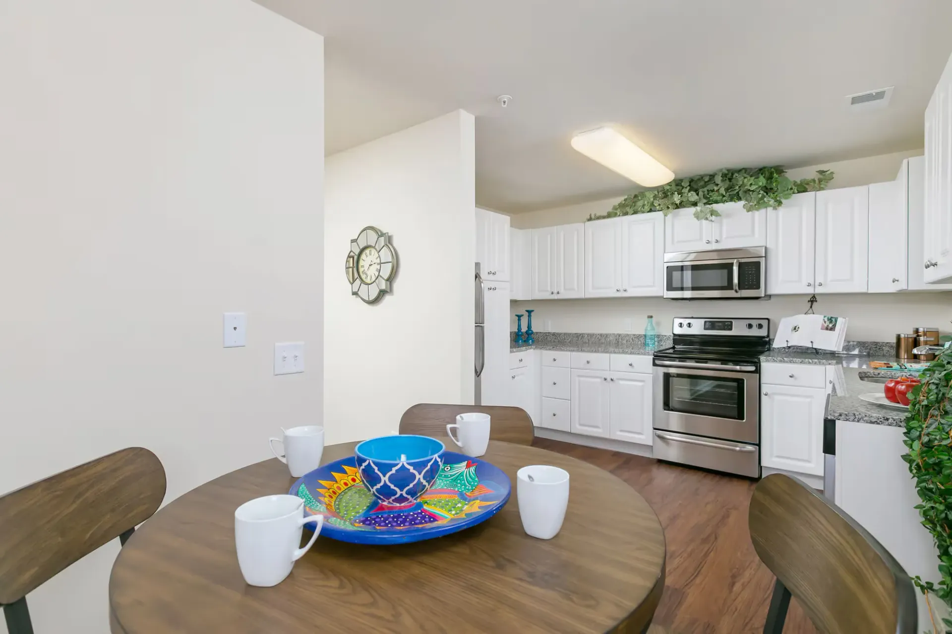 Bright white kitchen with stainless steel stove and microwave, white cabinets, and a round wooden dining table.