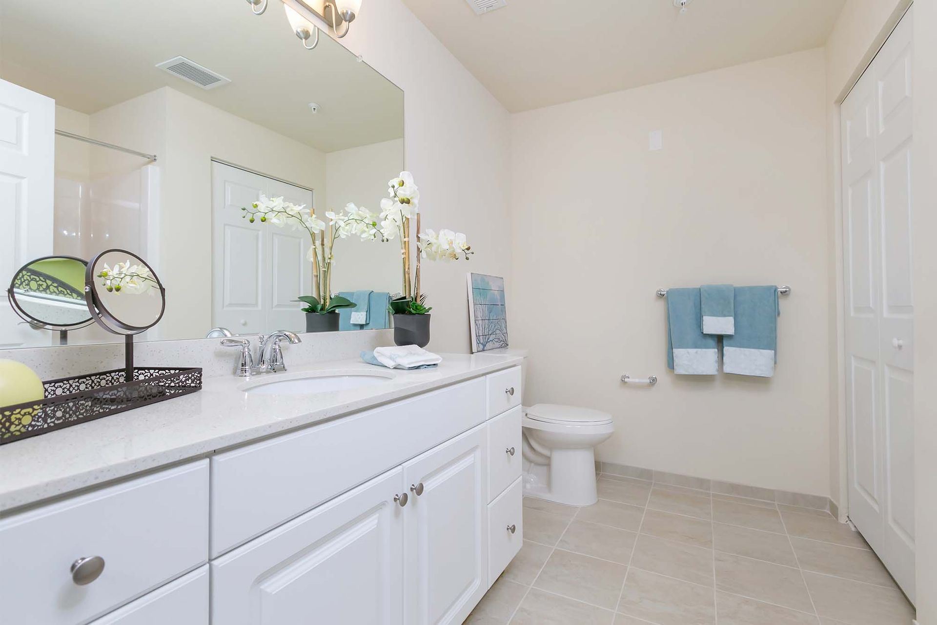 Bright bathroom with white vanity, large mirror, toilet, and teal towels.