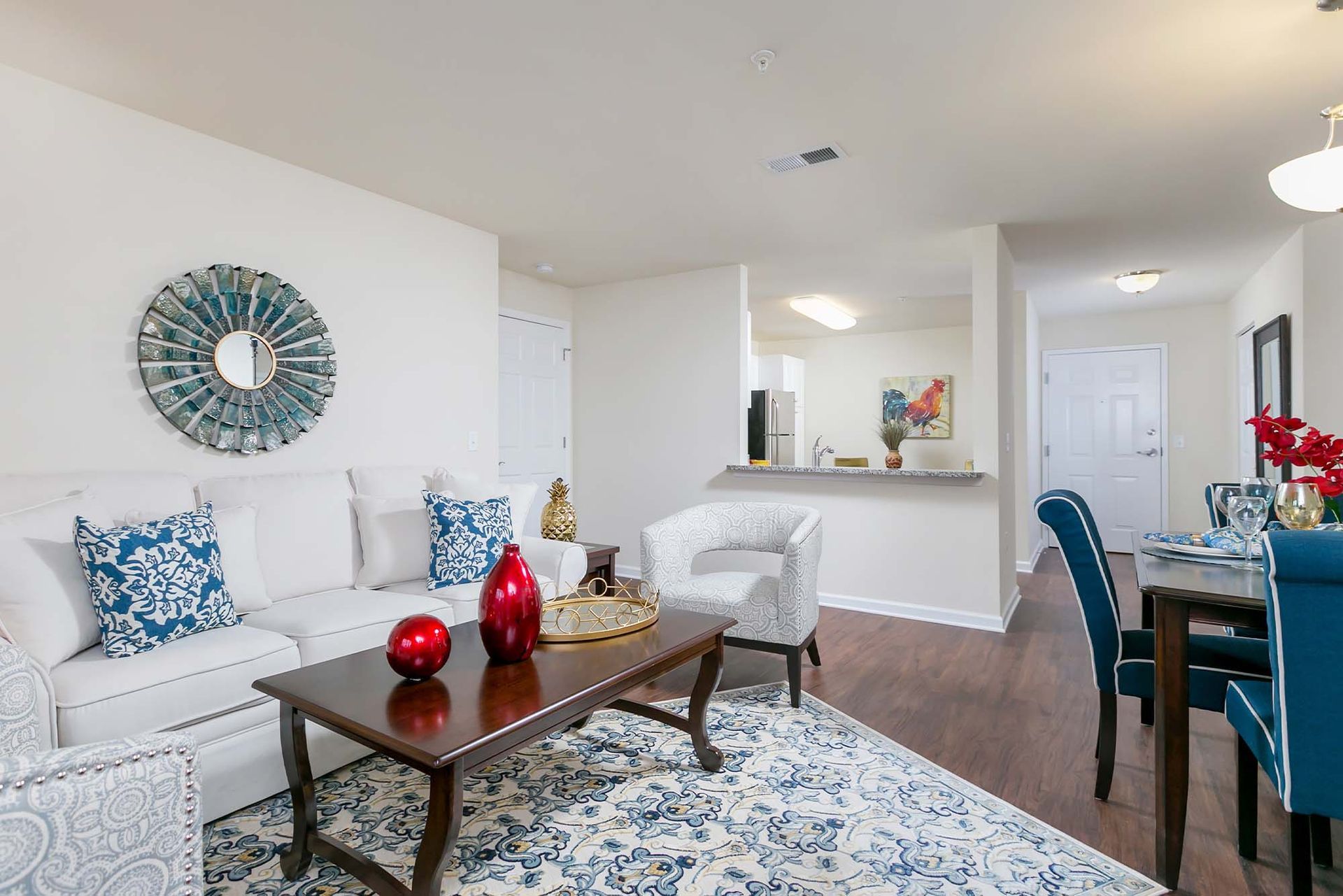 Bright living room with white sofa, decorative pillows, a patterned blue rug, and an open kitchen pass-through.
