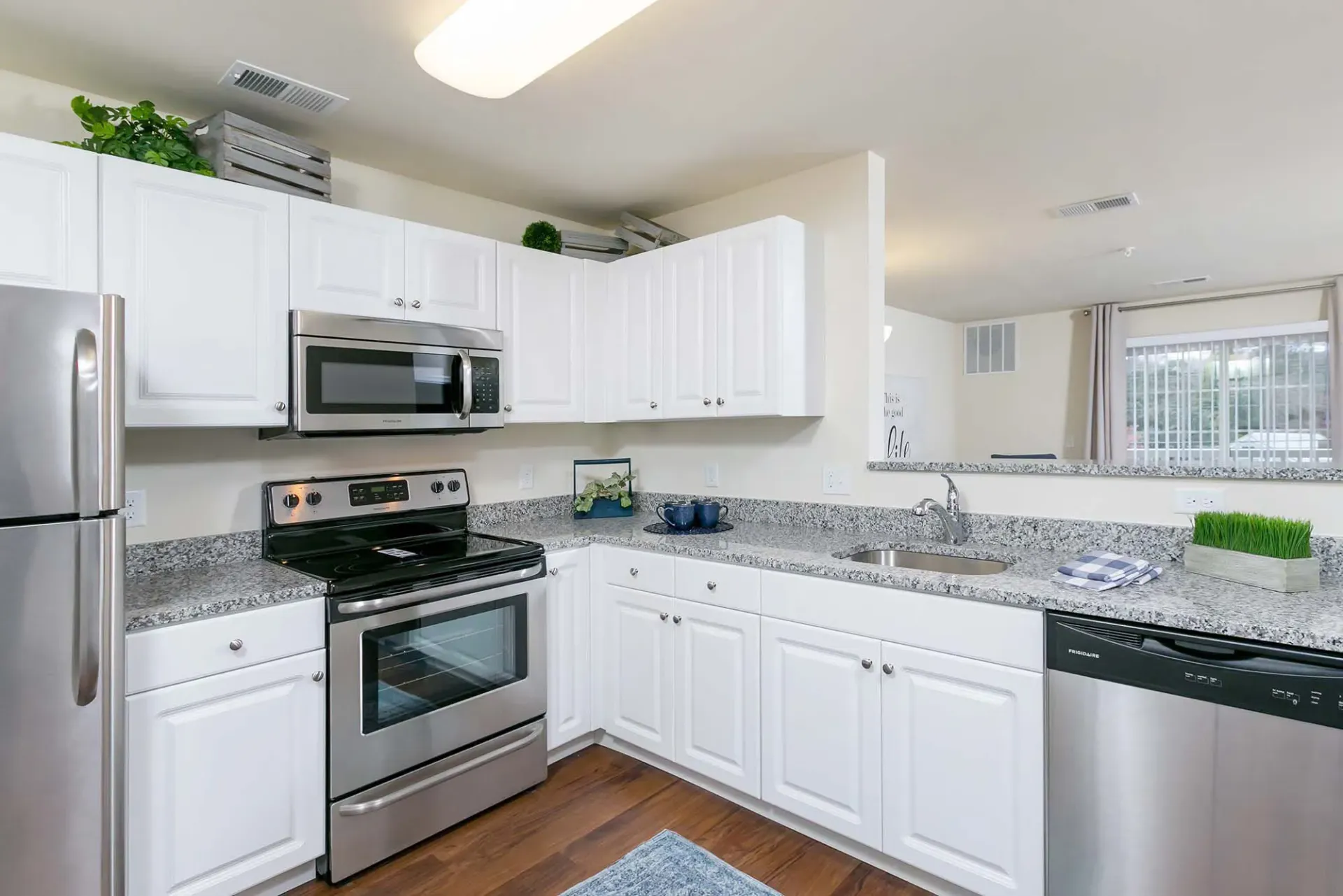 Modern white kitchen with granite countertops, stainless steel appliances, and a double sink.