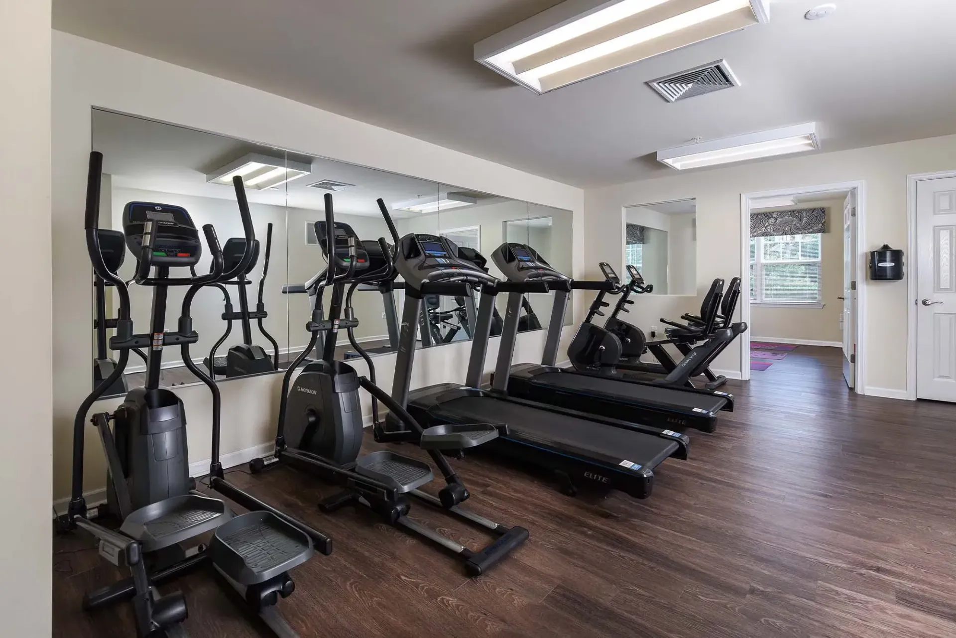 Cardio fitness room in apartment community with treadmills, ellipticals, and stationary bikes.