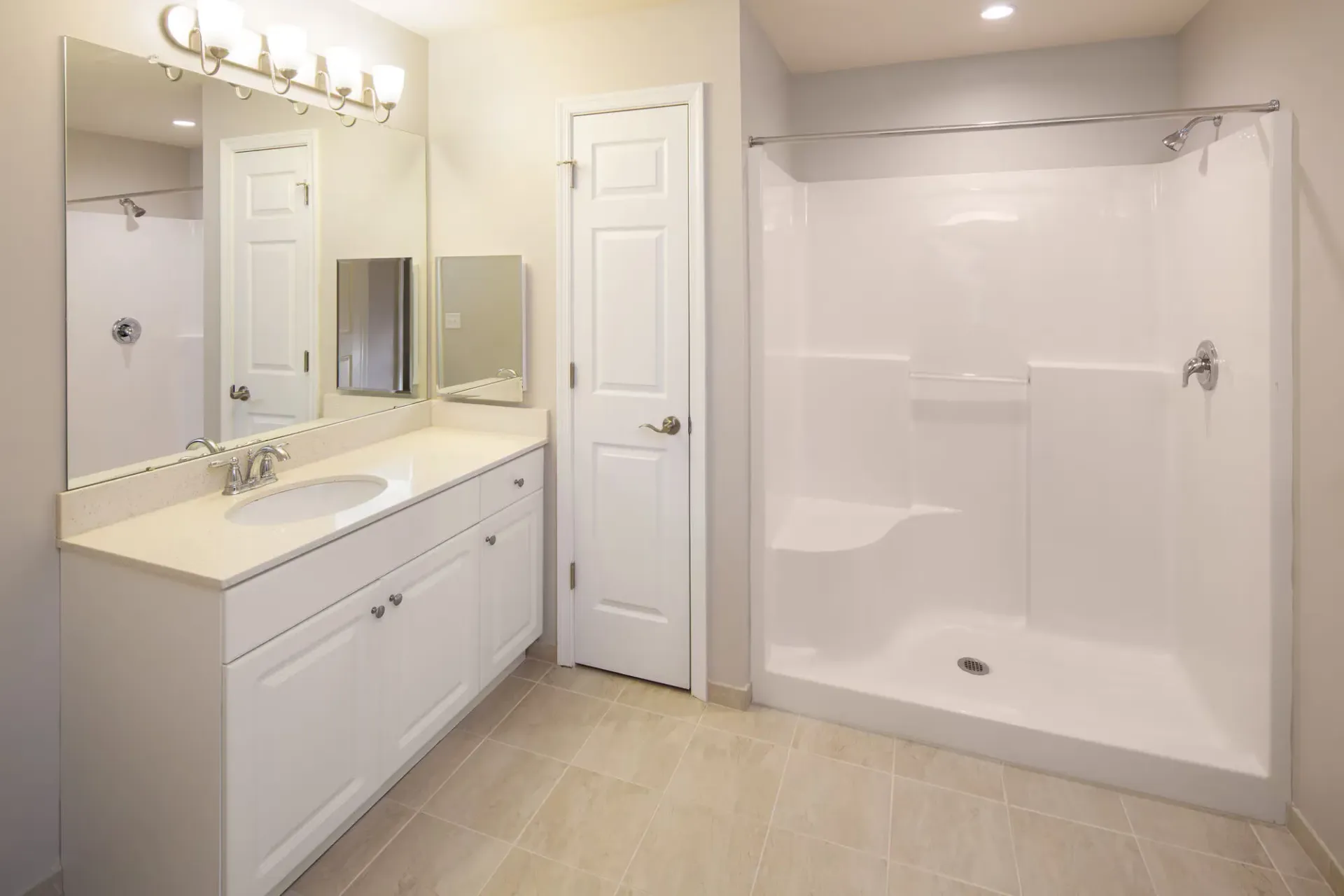 Bright apartment bathroom with white vanity, large mirror, and a shower-tub combo.
