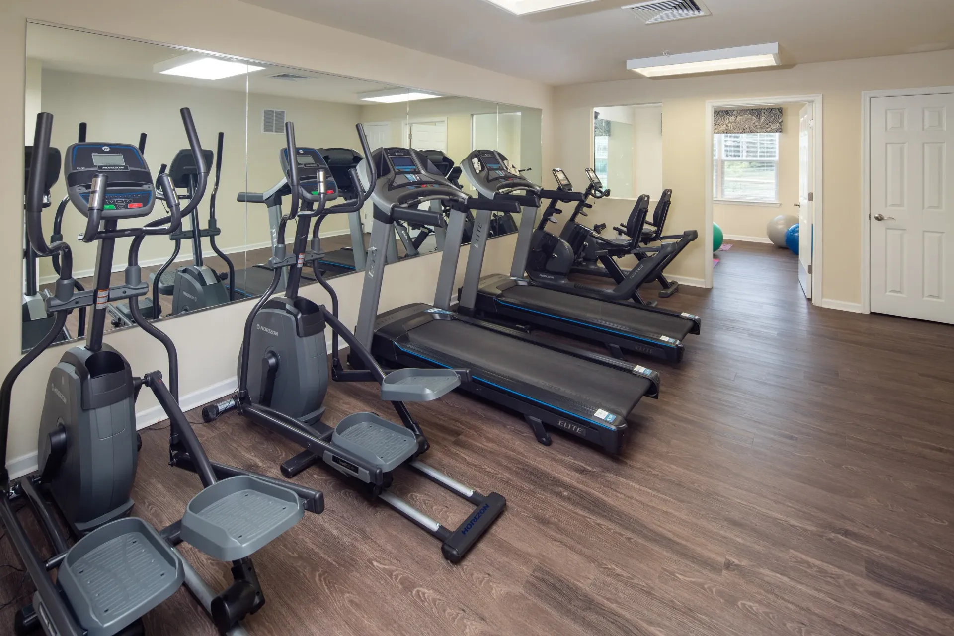 Fitness center with treadmills and ellipticals along a mirrored wall.