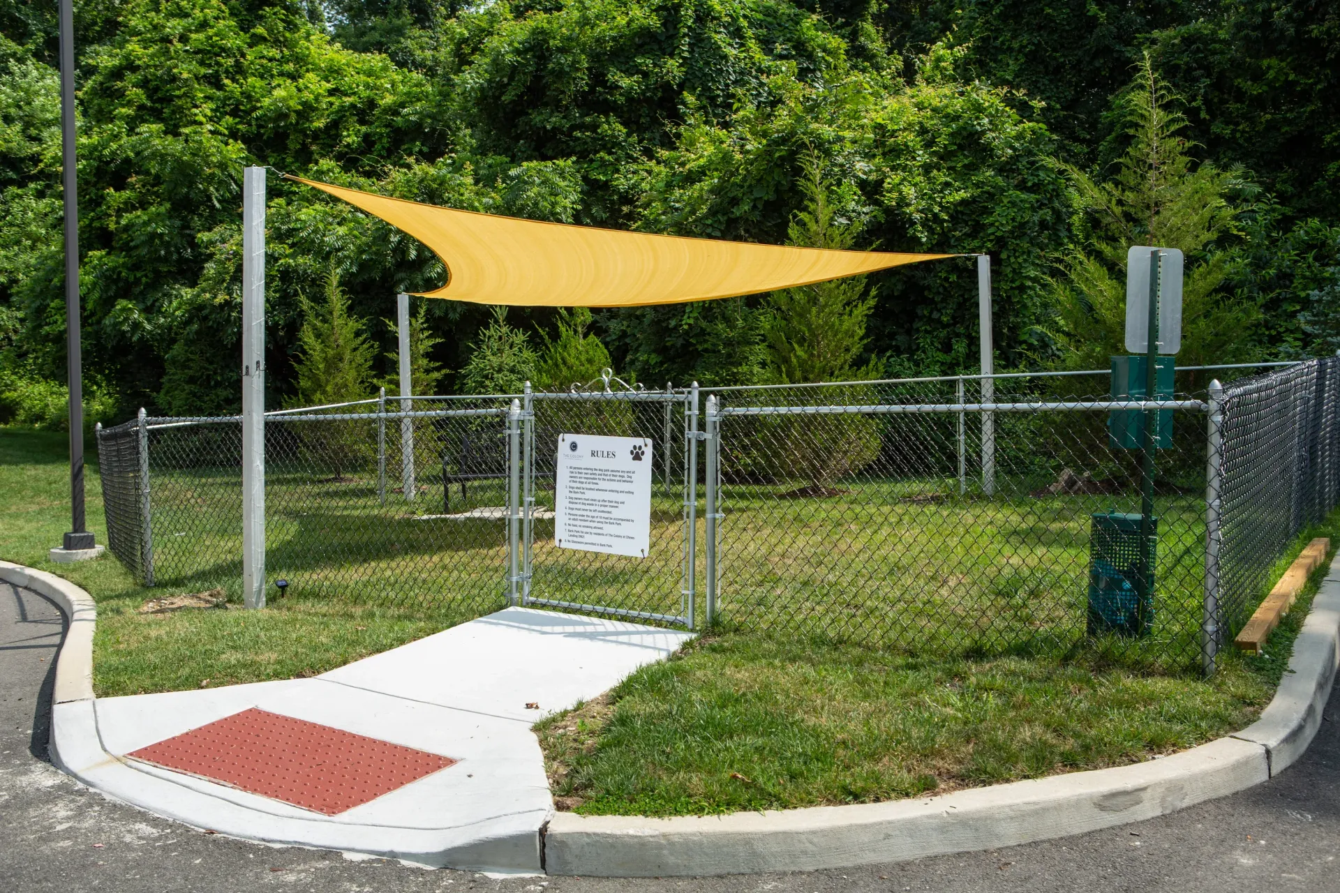 Fenced grassy outdoor amenity area with a yellow shade sail and rules sign.