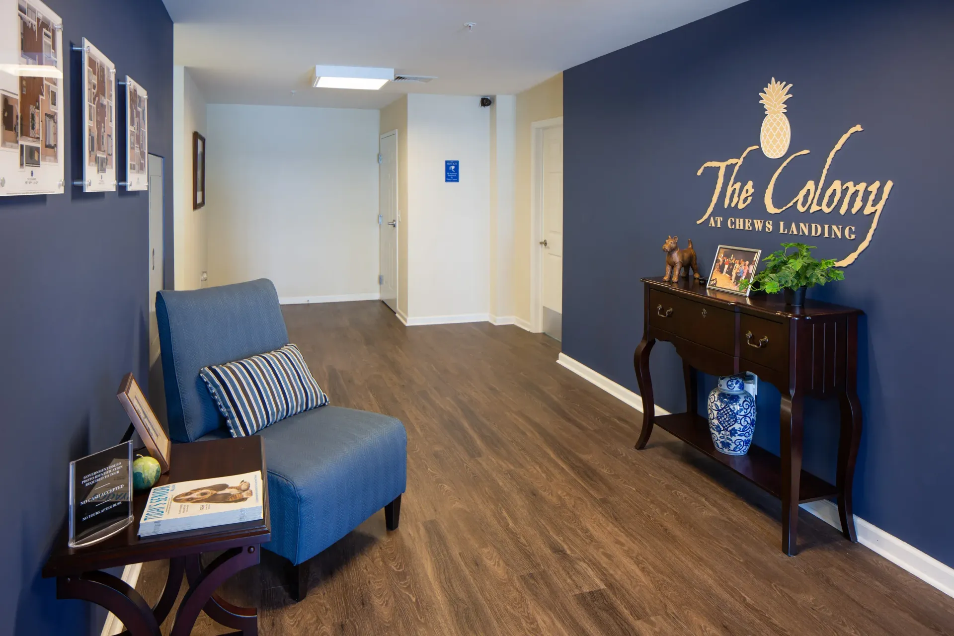 Interior lobby area with blue walls, a blue chair, and a console table near The Colony logo.