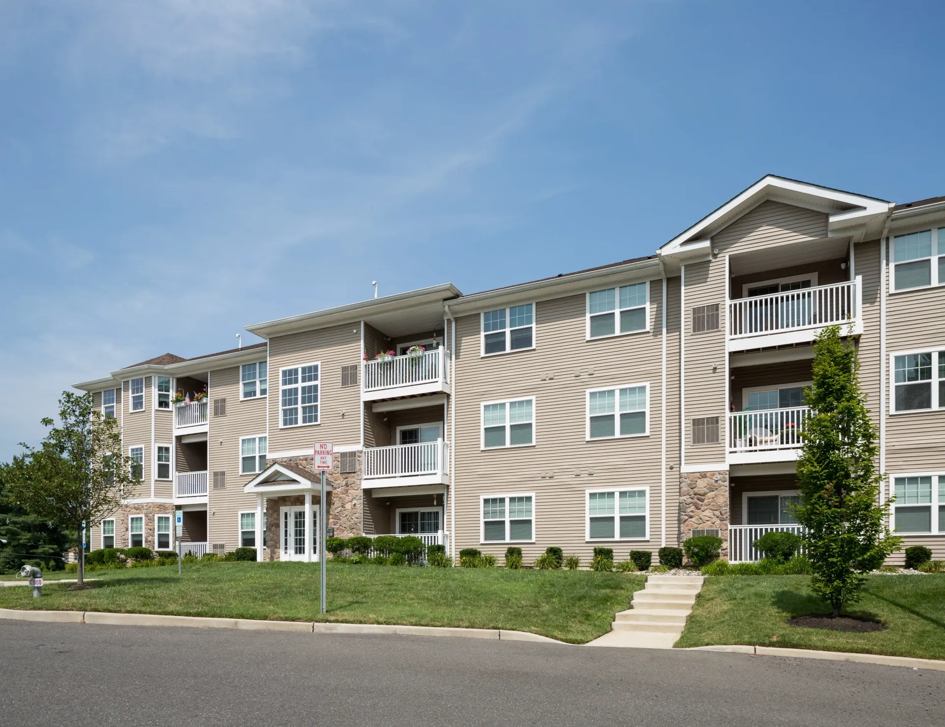 Exterior view of a beige apartment building with balconies and a manicured lawn.