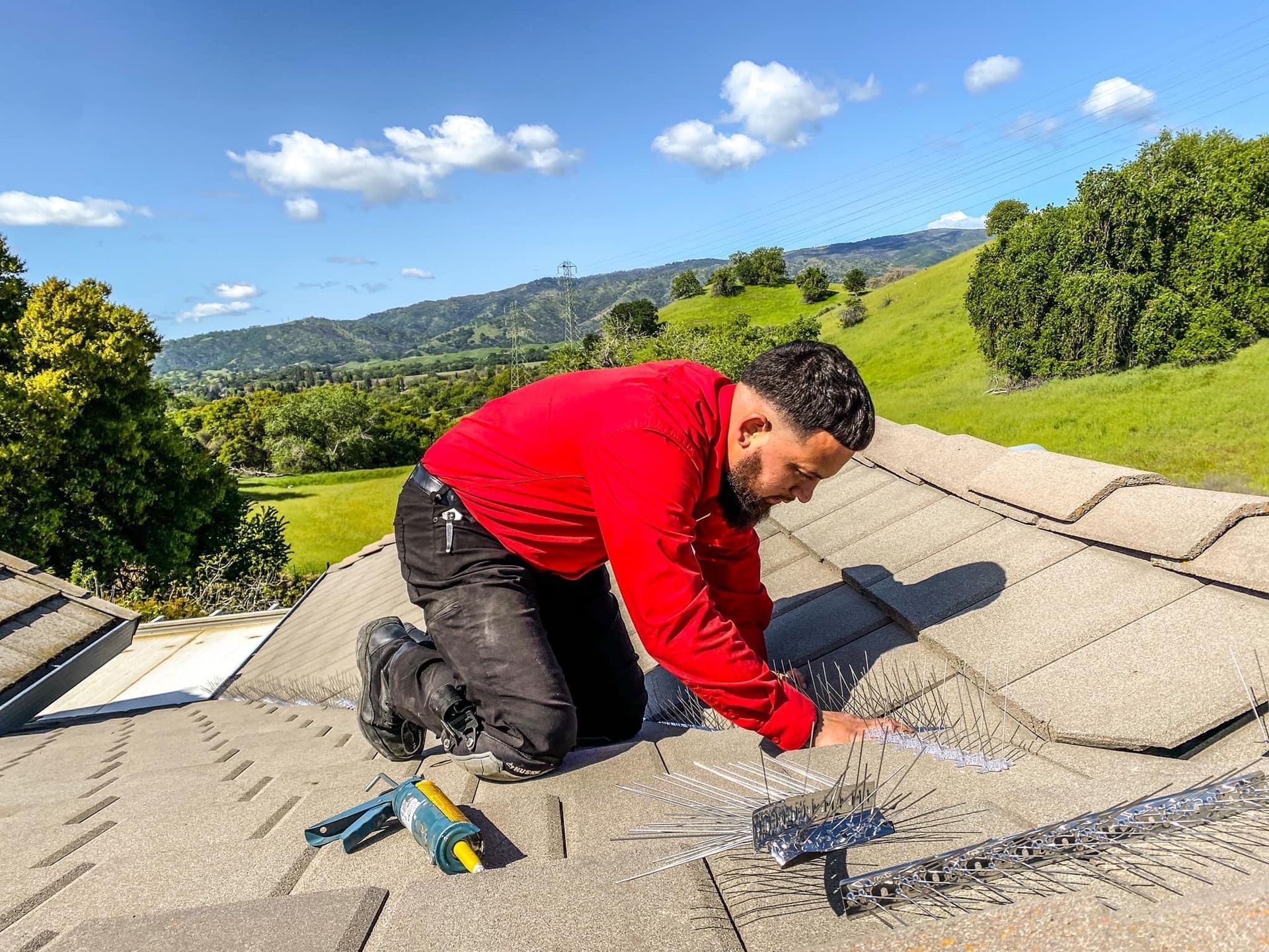 A man in a red shirt is kneeling on top of a roof.