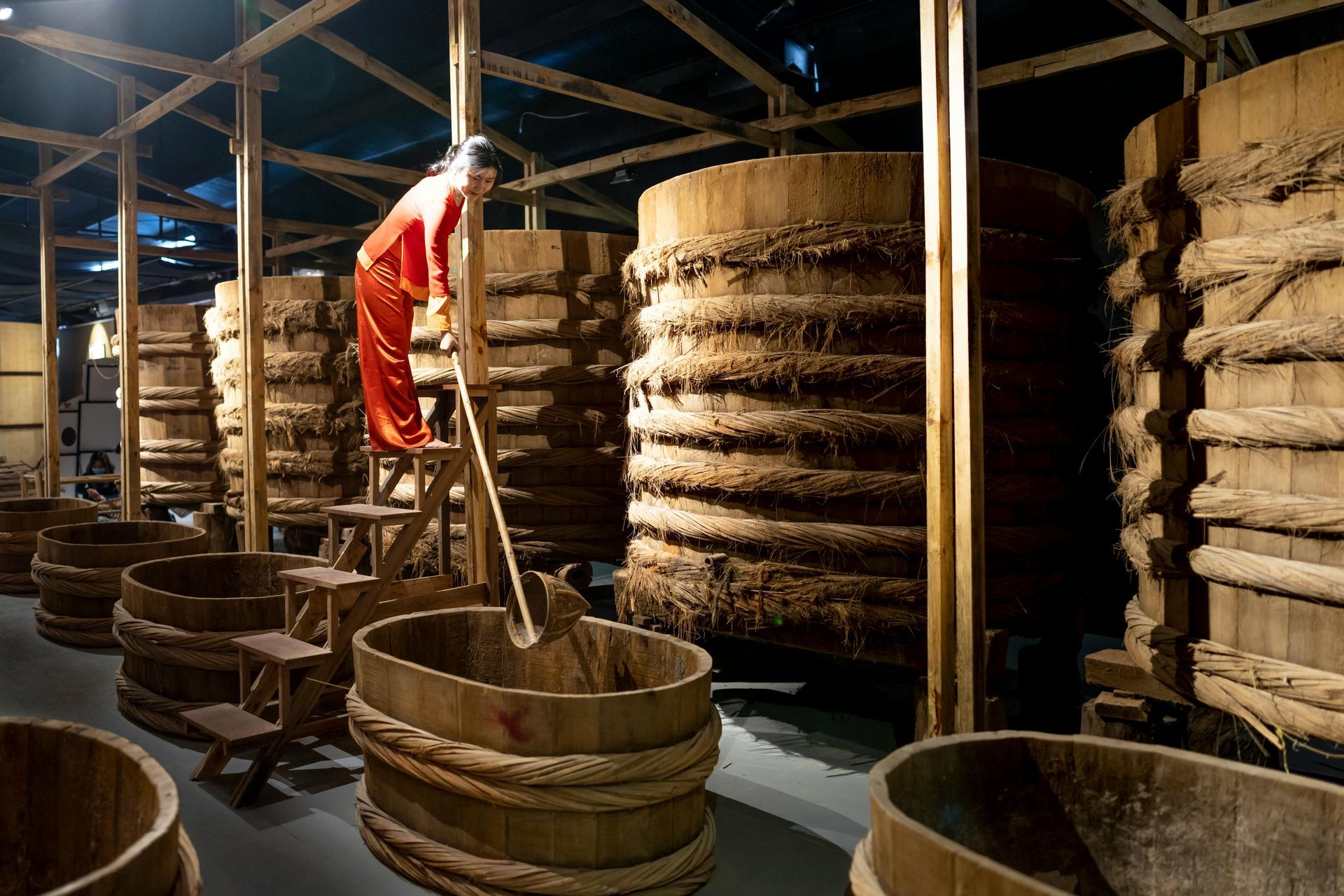 A woman is standing on a ladder in a room filled with wooden barrels.