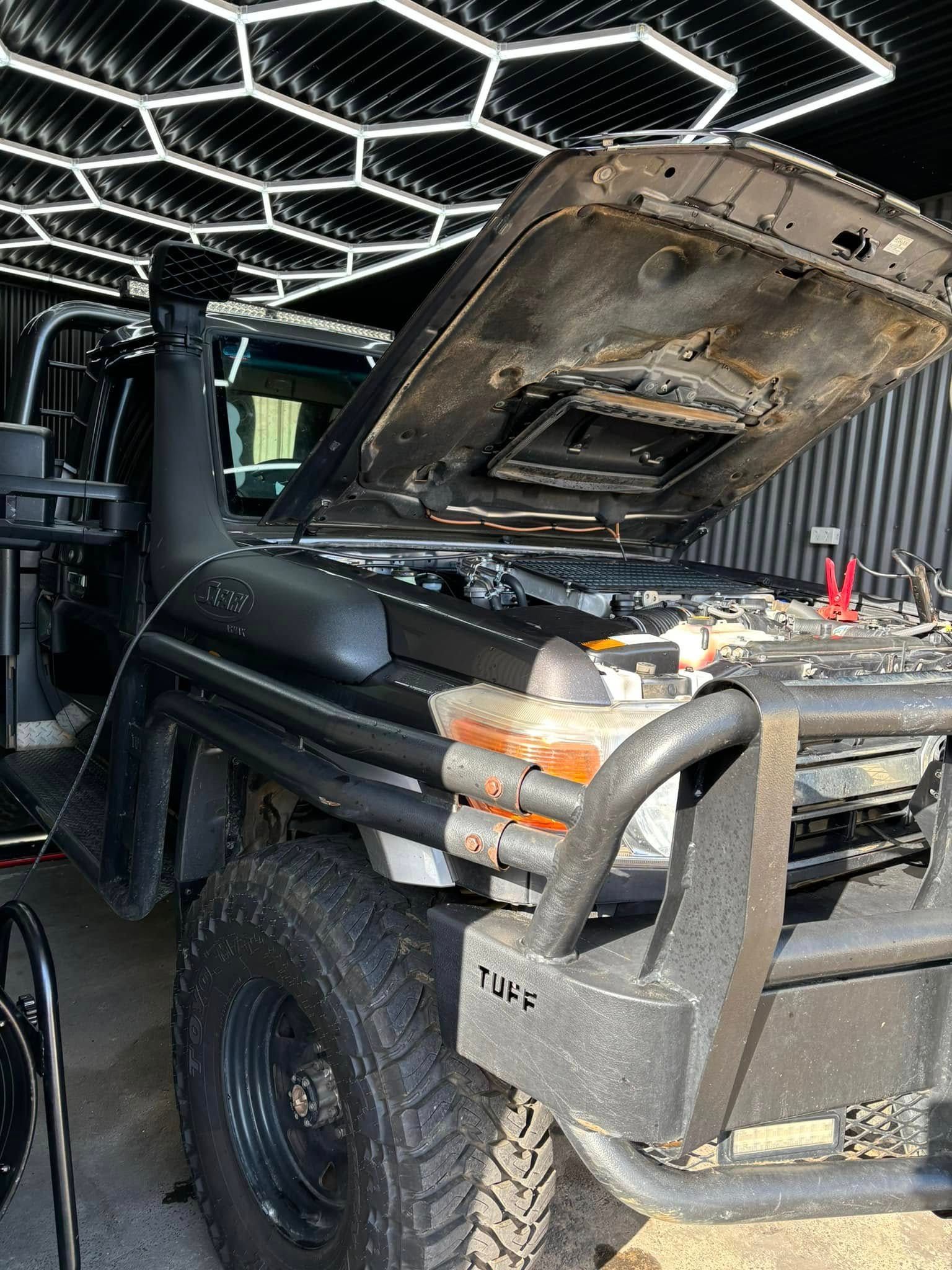 A black truck with the hood up is parked in a garage.