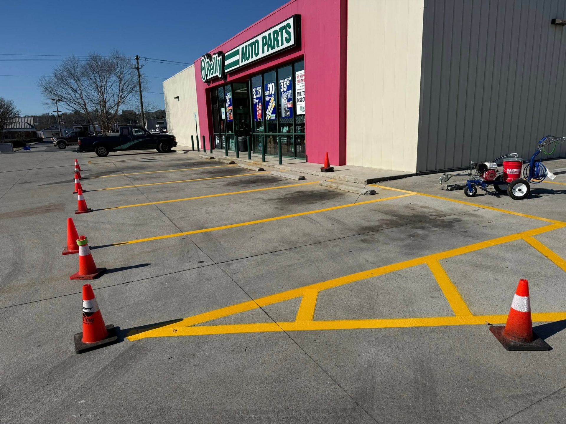 Yellow parking lines being painted in front of an auto parts store with orange cones in place.