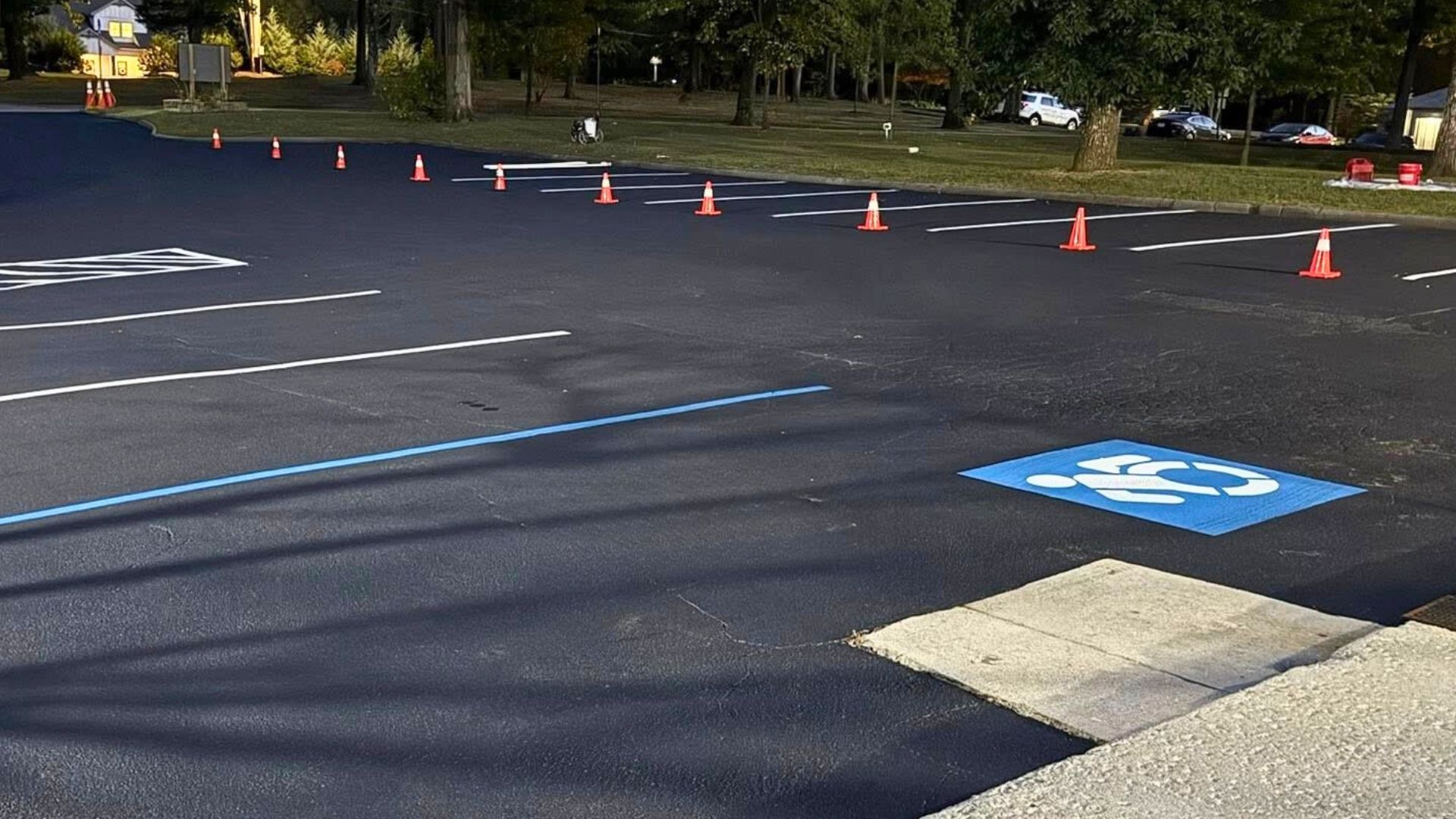 Asphalt parking lot with blue handicap space symbol and orange cones. White lines mark parking spaces.