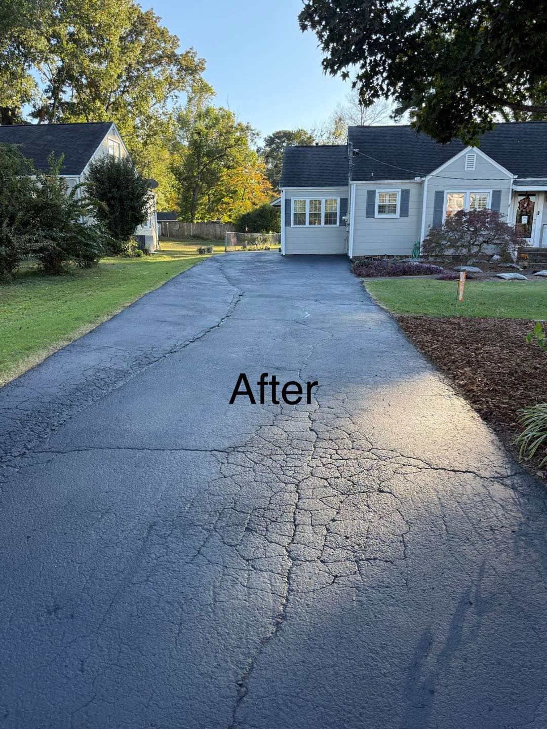 Asphalt driveway after repair, in front of a blue house with landscaping and green grass.