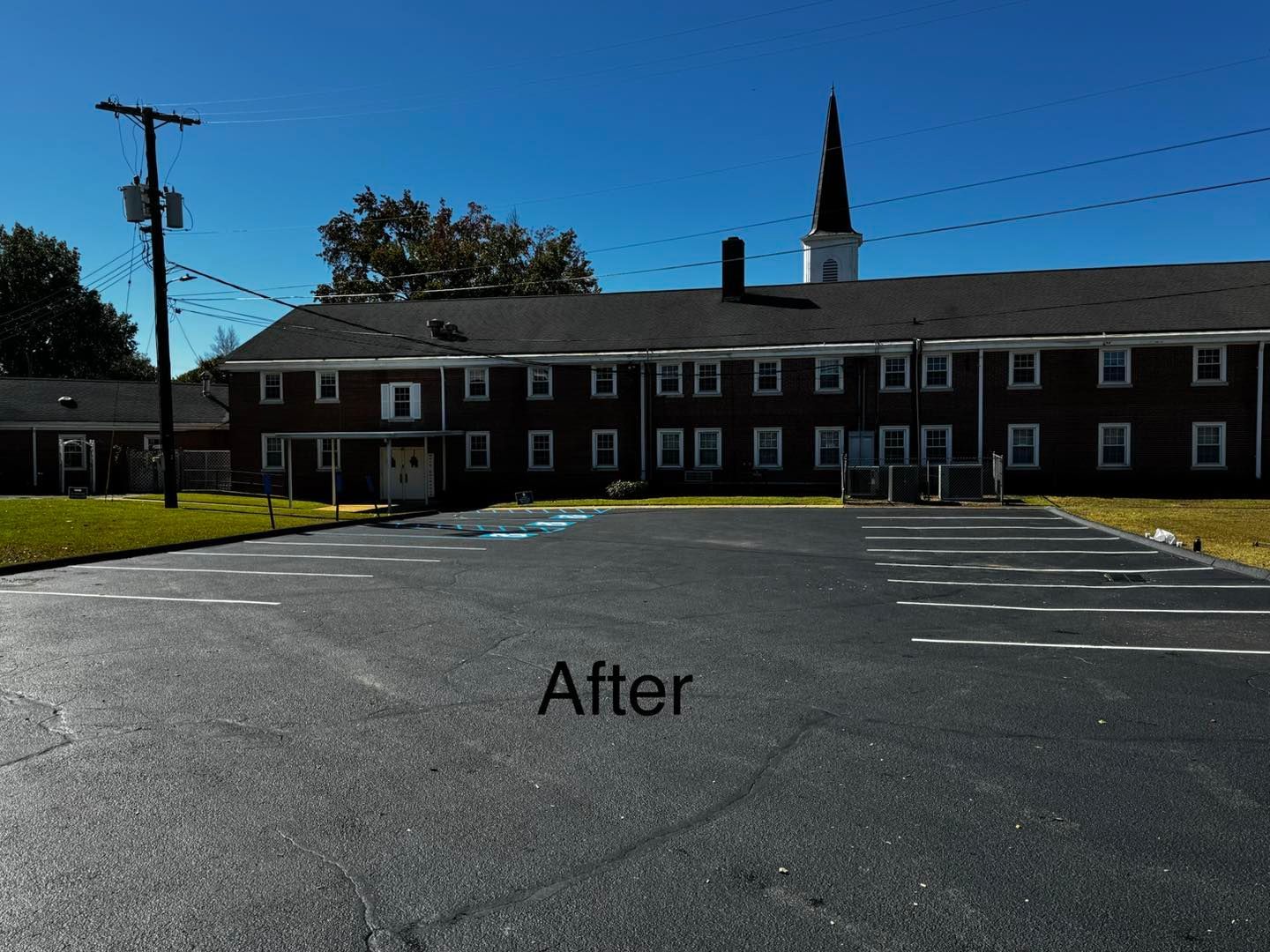 Exterior view of a dark asphalt parking lot in front of a brick building with a church steeple.
