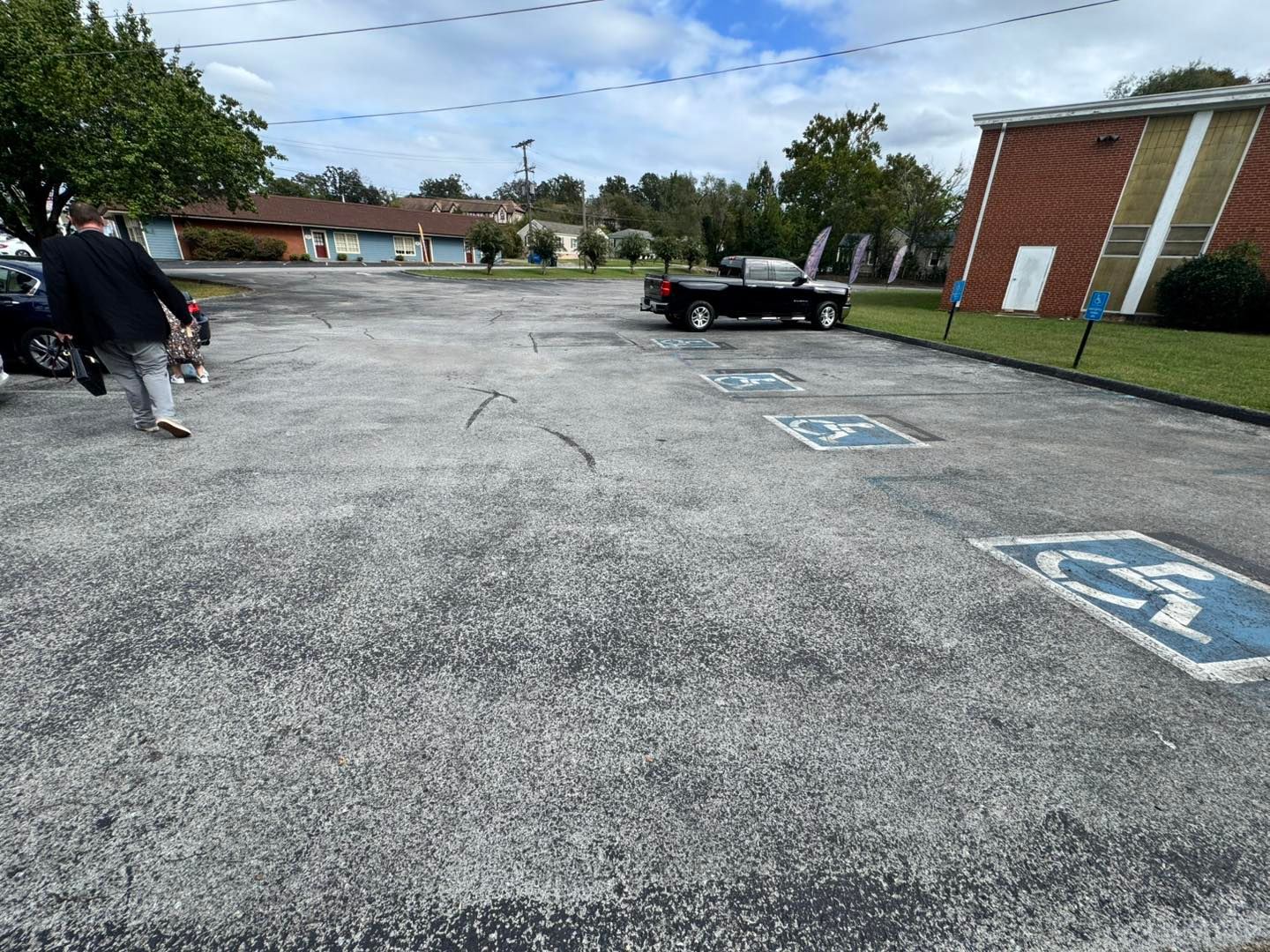 Parking lot with a person walking, marked handicap spaces, and a red brick building.