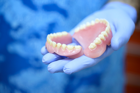 A person wearing blue medical gloves holding a pair of complete dentures.
