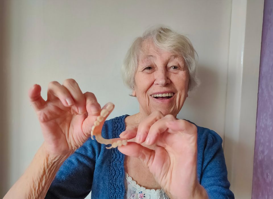 A person holds a dental bridge device in both hands, smiling in front of a neutral background.