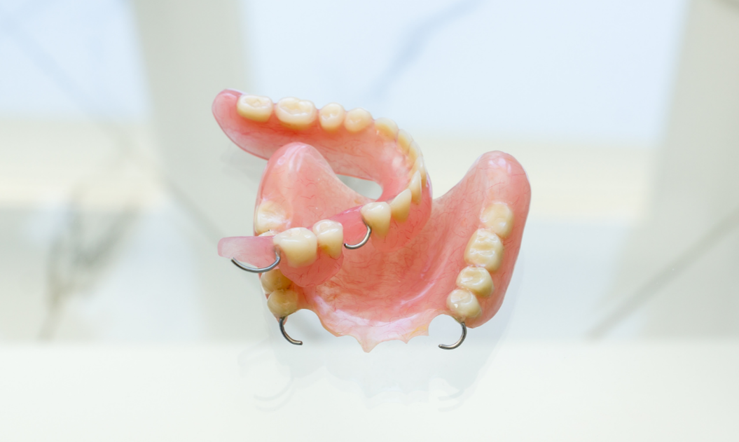 A partial denture appliance with two artificial teeth and metal clasps, showing the pink acrylic base and wire hooks.