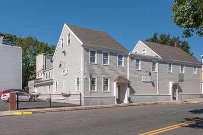 Gray multi-story building with a light blue sky and some cars parked on the side of the road.