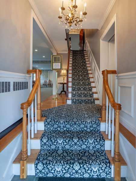 Staircase in a home with patterned carpet and wooden handrails, lit by a chandelier.