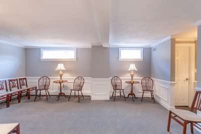 Empty waiting room with chairs, tables, lamps, and windows, painted in white and gray.