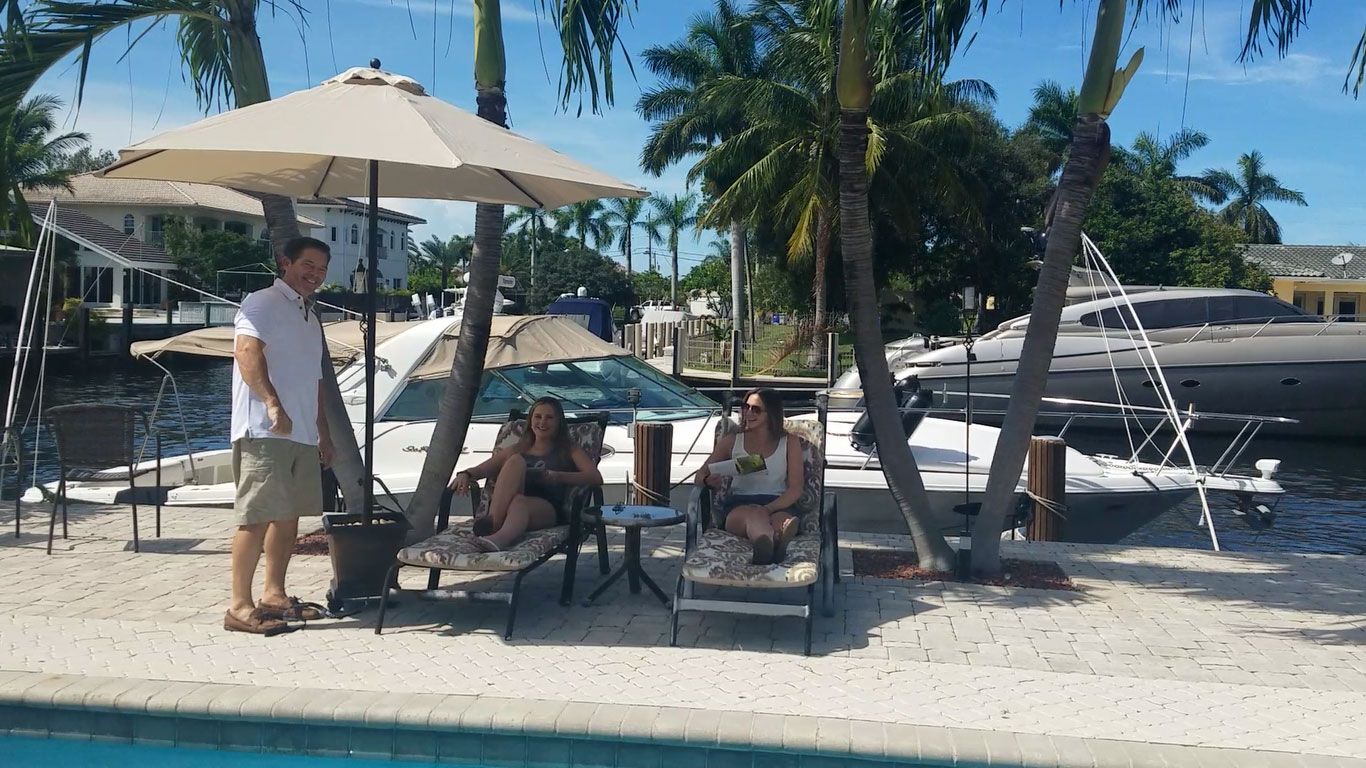 A group of people are sitting under umbrellas near a pool.