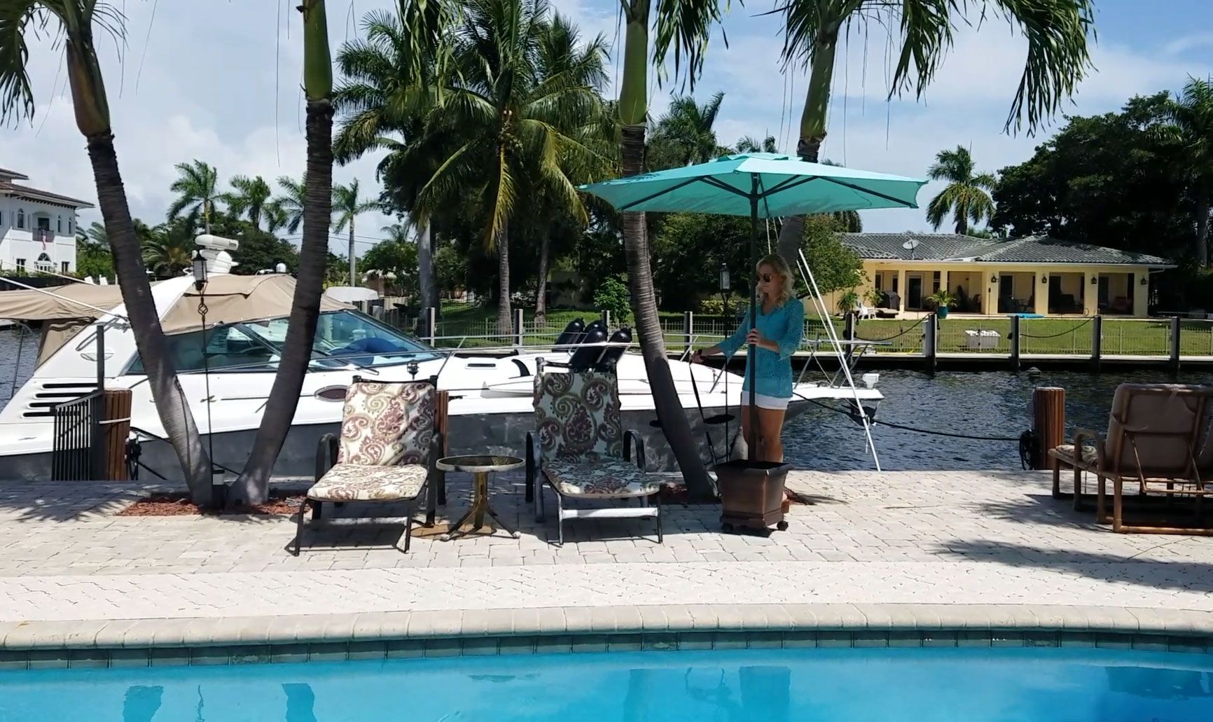 A woman stands under an umbrella next to a swimming pool