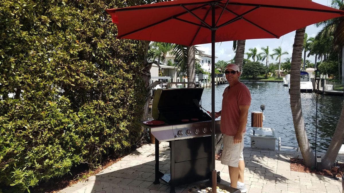 A man is standing in front of a grill under an umbrella.