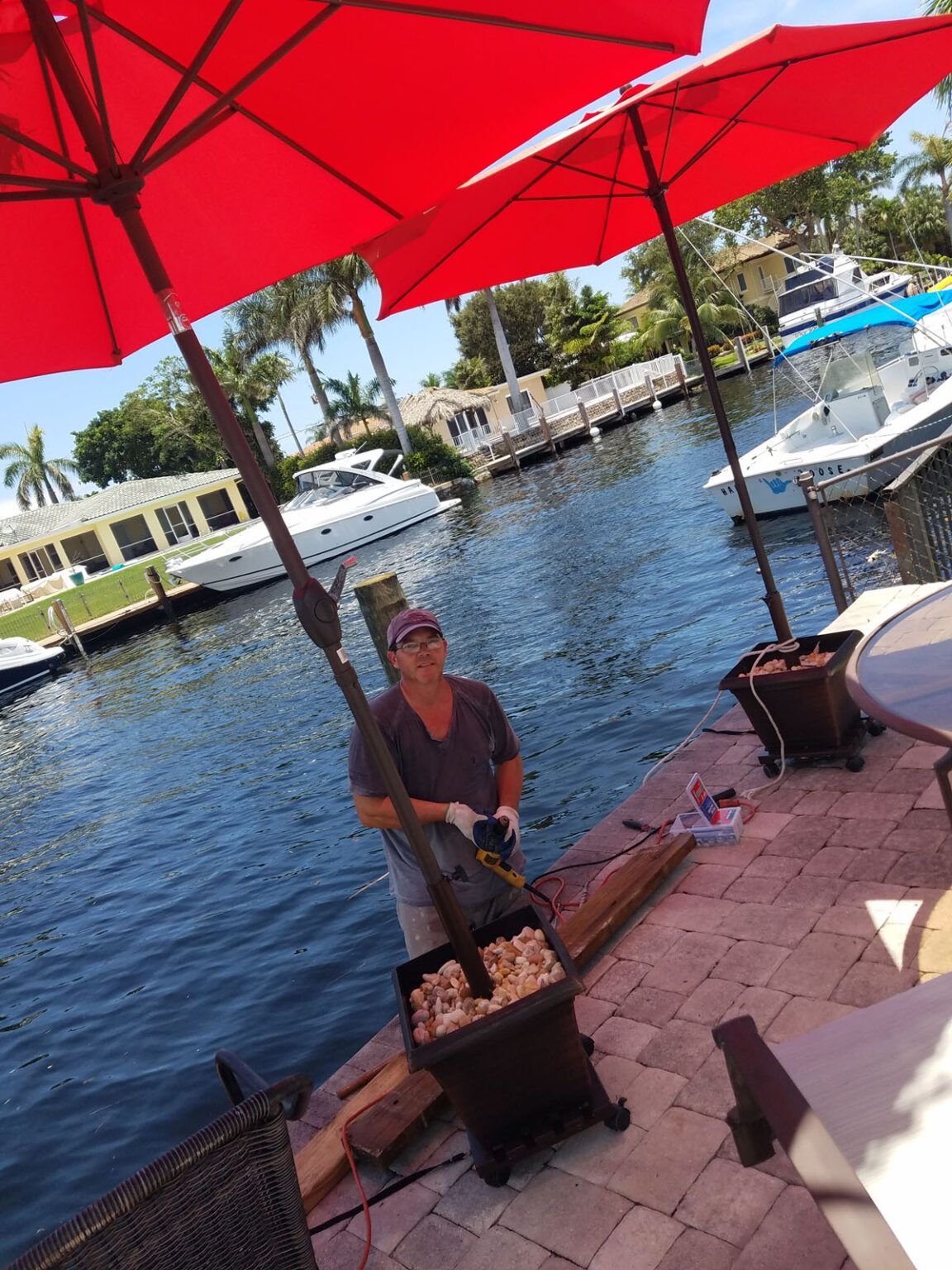 A man is standing under a red umbrella in front of a body of water