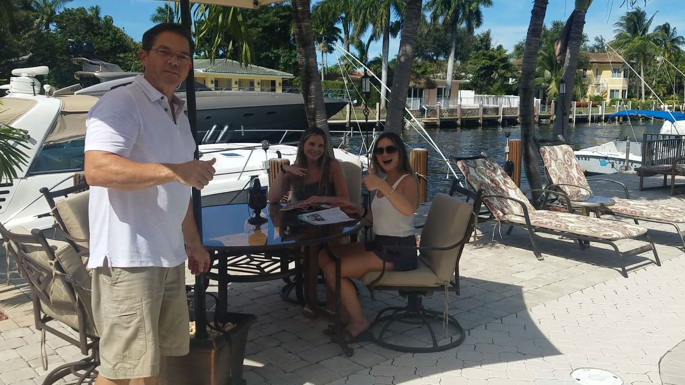 A man and two women are sitting at a table on the beach