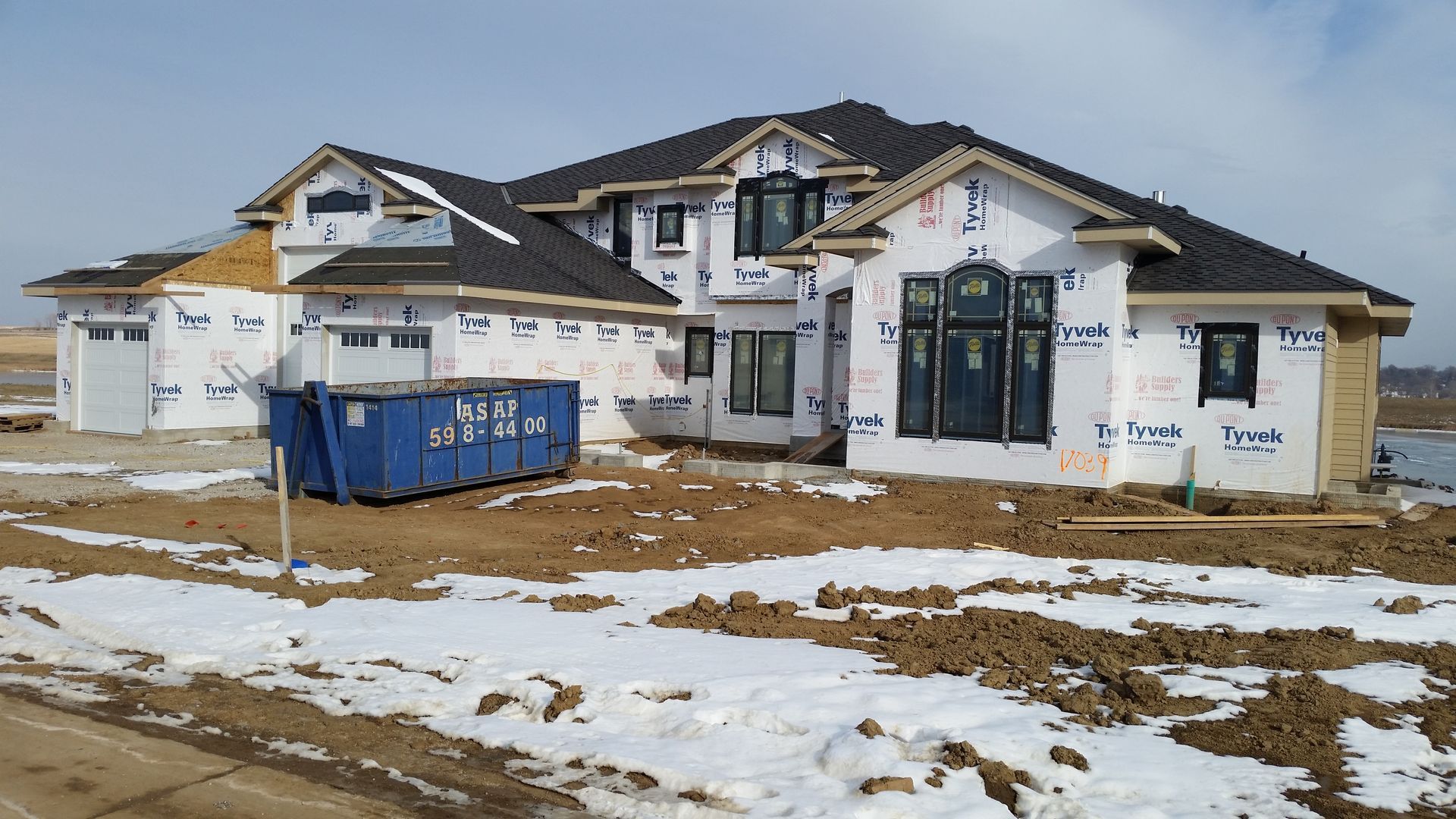 A blue dumpster is sitting in a driveway next to a house under construction.