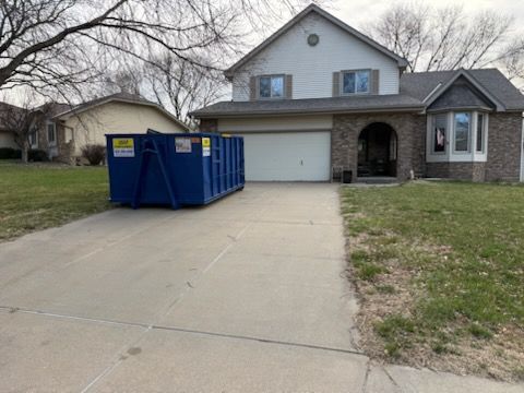 A blue dumpster is sitting in a driveway next to a house.