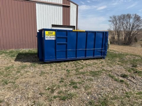 A large, empty blue dumpster positioned on a construction site near a building.