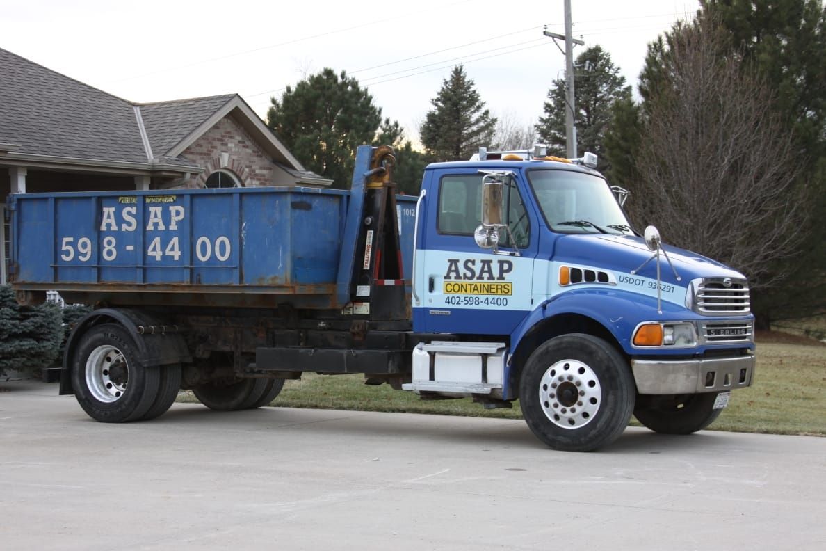 A blue asap dump truck is parked in front of a house