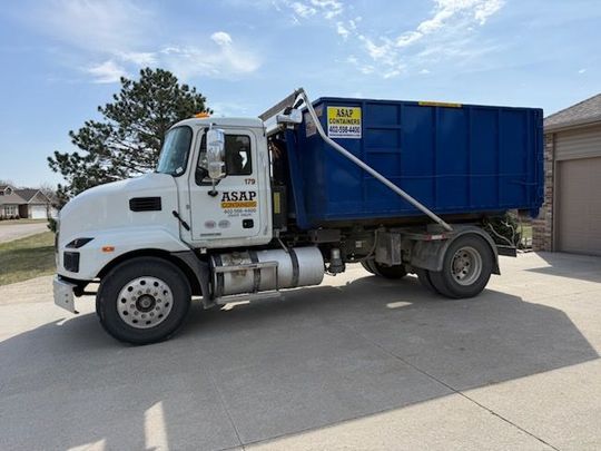 A large, empty blue dumpster positioned on a construction site near a building.