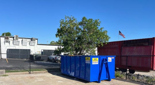 A large, empty blue dumpster positioned on a construction site near a building.