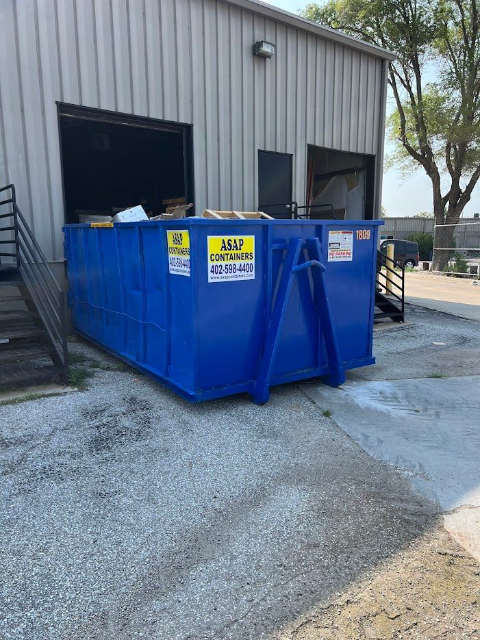 A blue dumpster rental is sitting in front of a building.