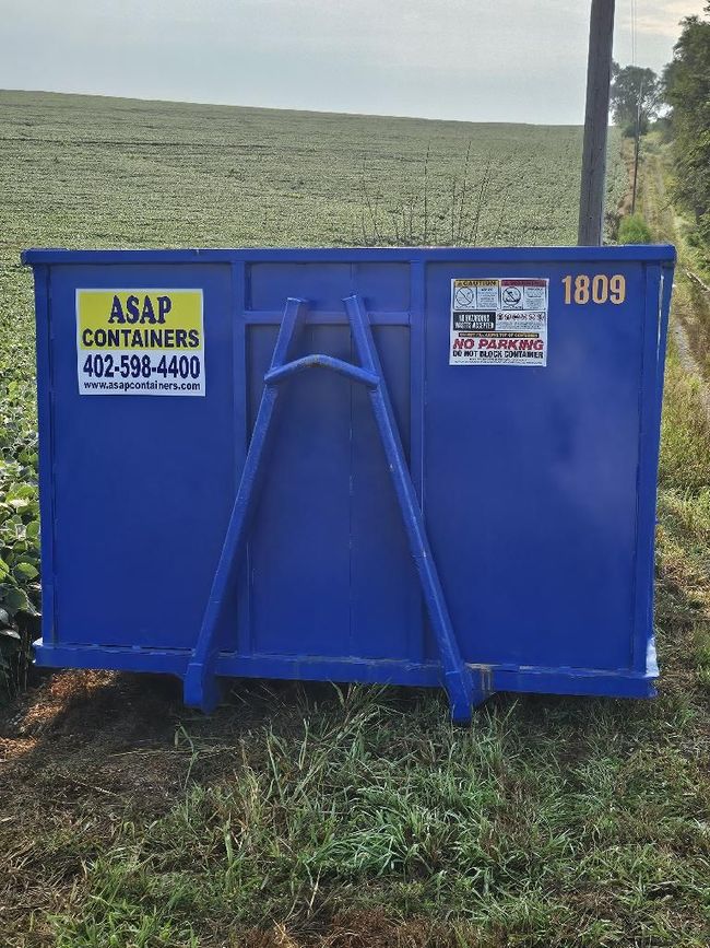 A blue dumpster is sitting in the middle of a grassy field.