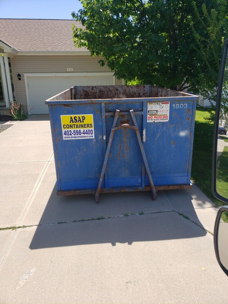 A blue dumpster is sitting in a driveway next to a house.