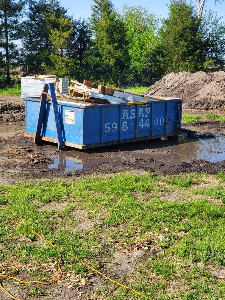 A blue dumpster rental is sitting in the middle of a grassy field.