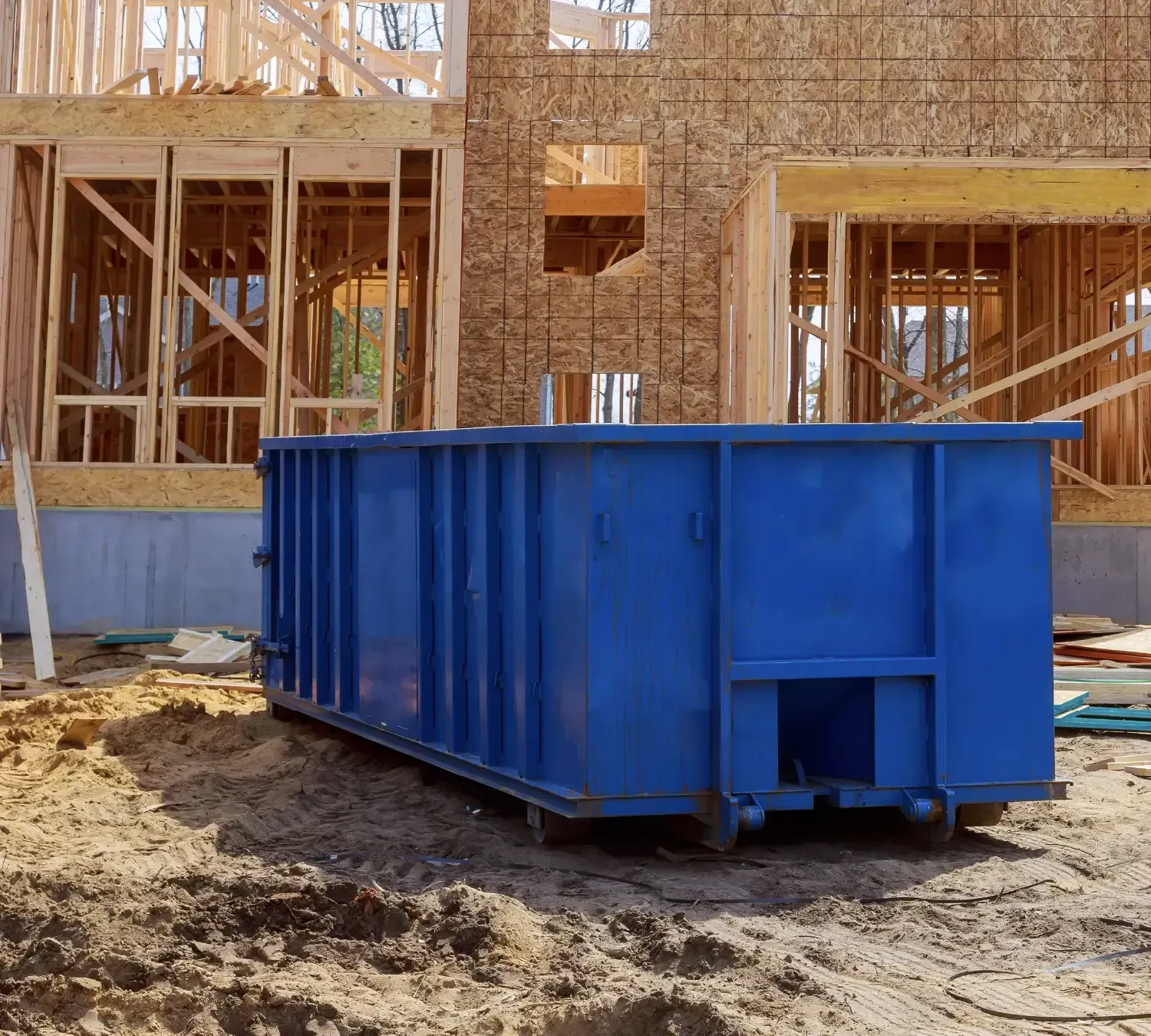 A large, empty blue dumpster positioned on a construction site near a building.
