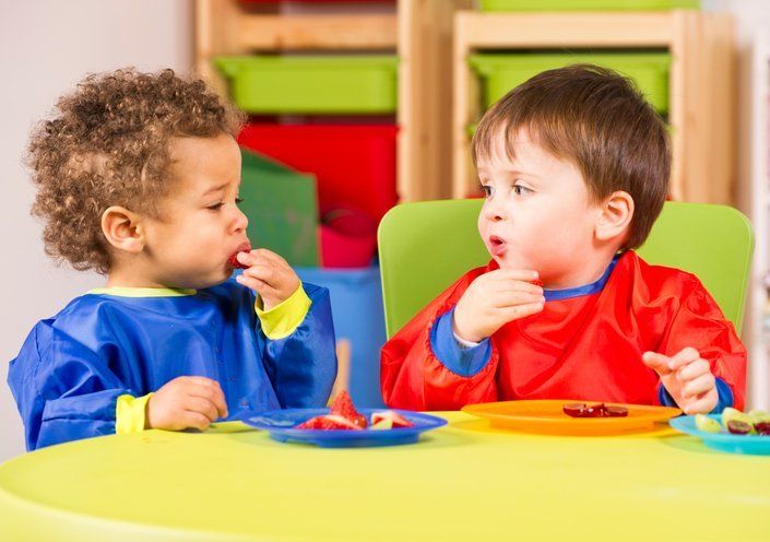 Two toddlers eating fruit in a nursery