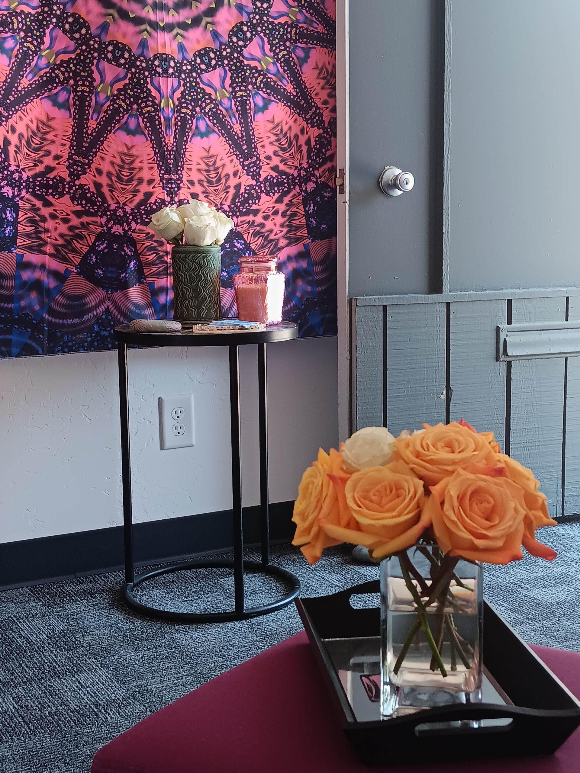 Arrangement of orange roses, white roses, a side table, and tapestry, in a room with blue carpet.