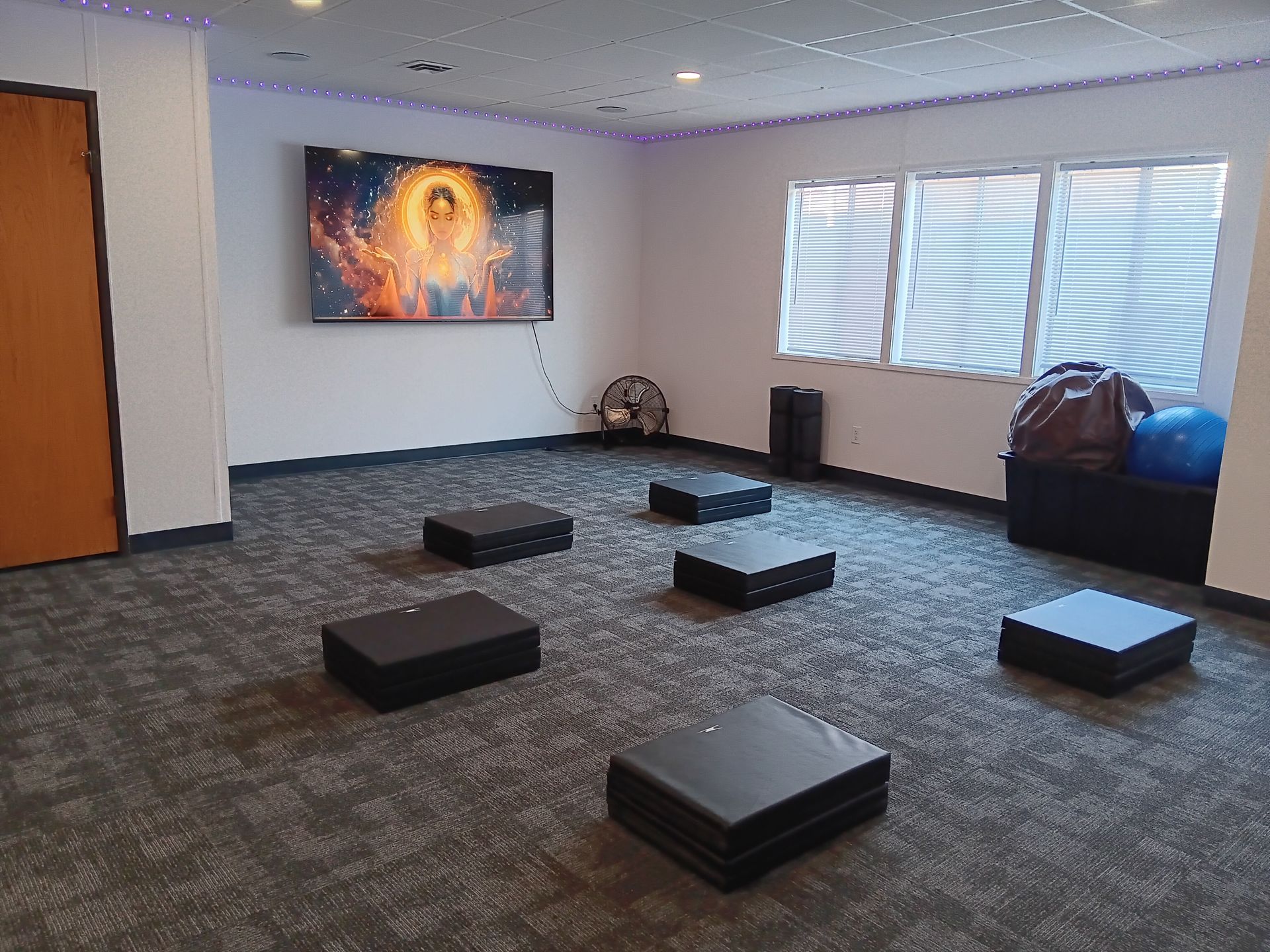 Room with six black platforms on the floor, a painting on the wall, and a window with blinds.