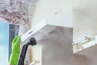A woman wearing yellow gloves is cleaning a hood in a kitchen. A woman wearing yellow gloves is cleaning a hood in a kitchen.