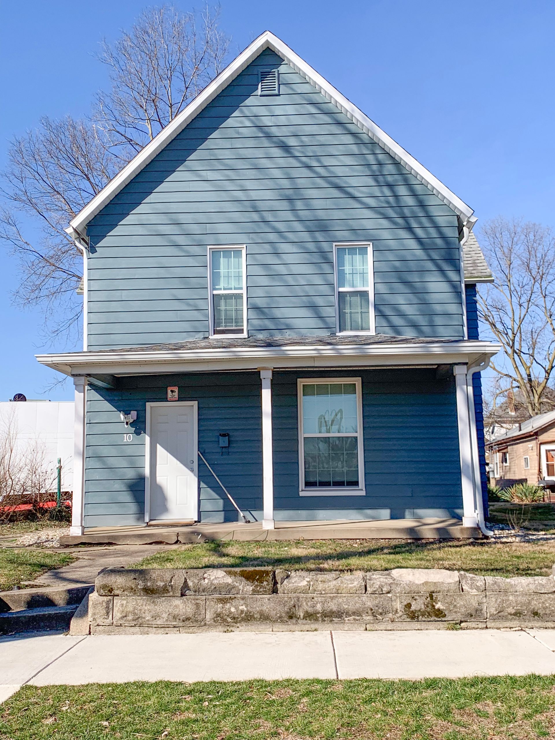A blue house with a white porch and a blue sky in the background