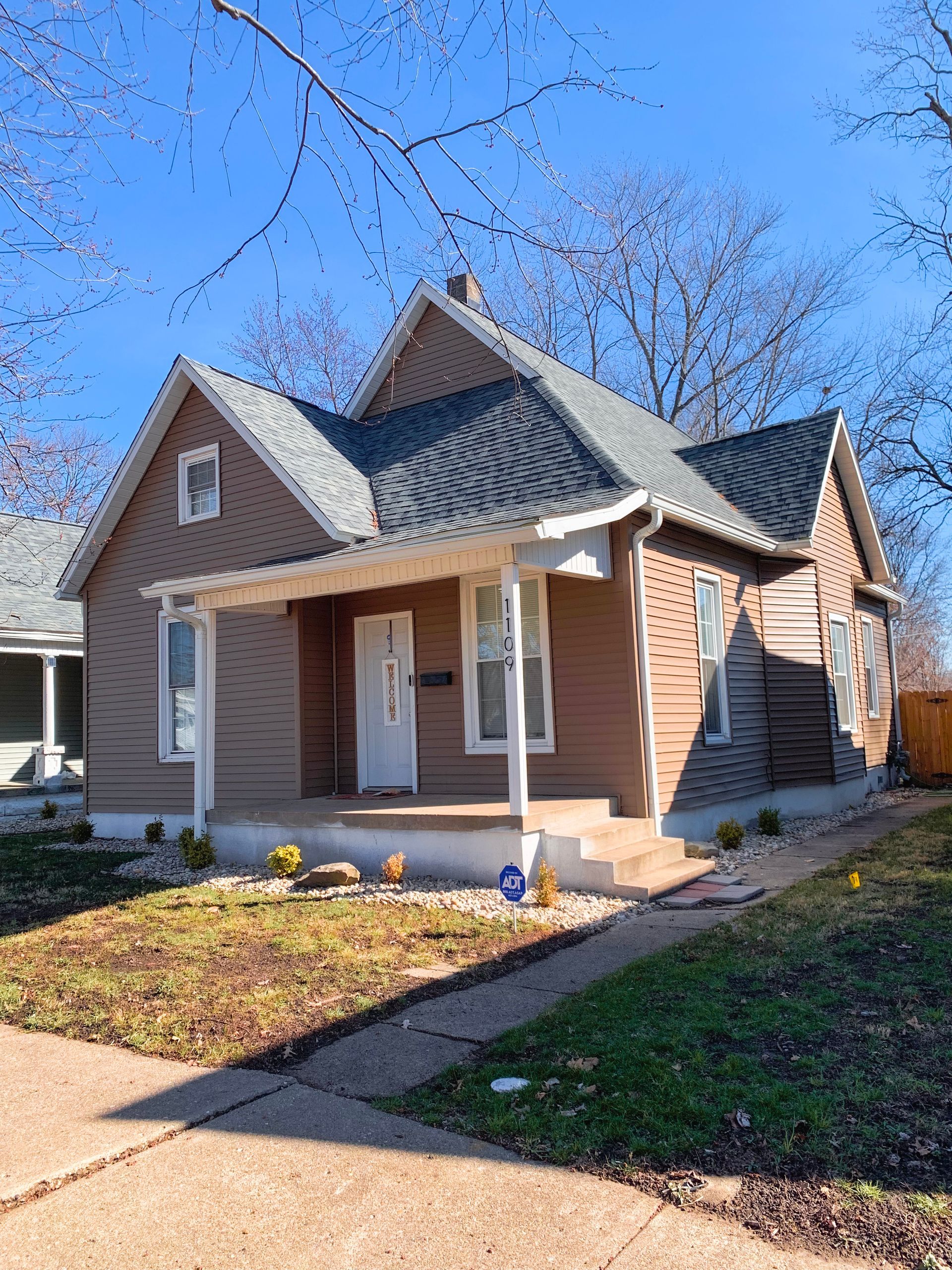 A small brown house with a gray roof and a porch.
