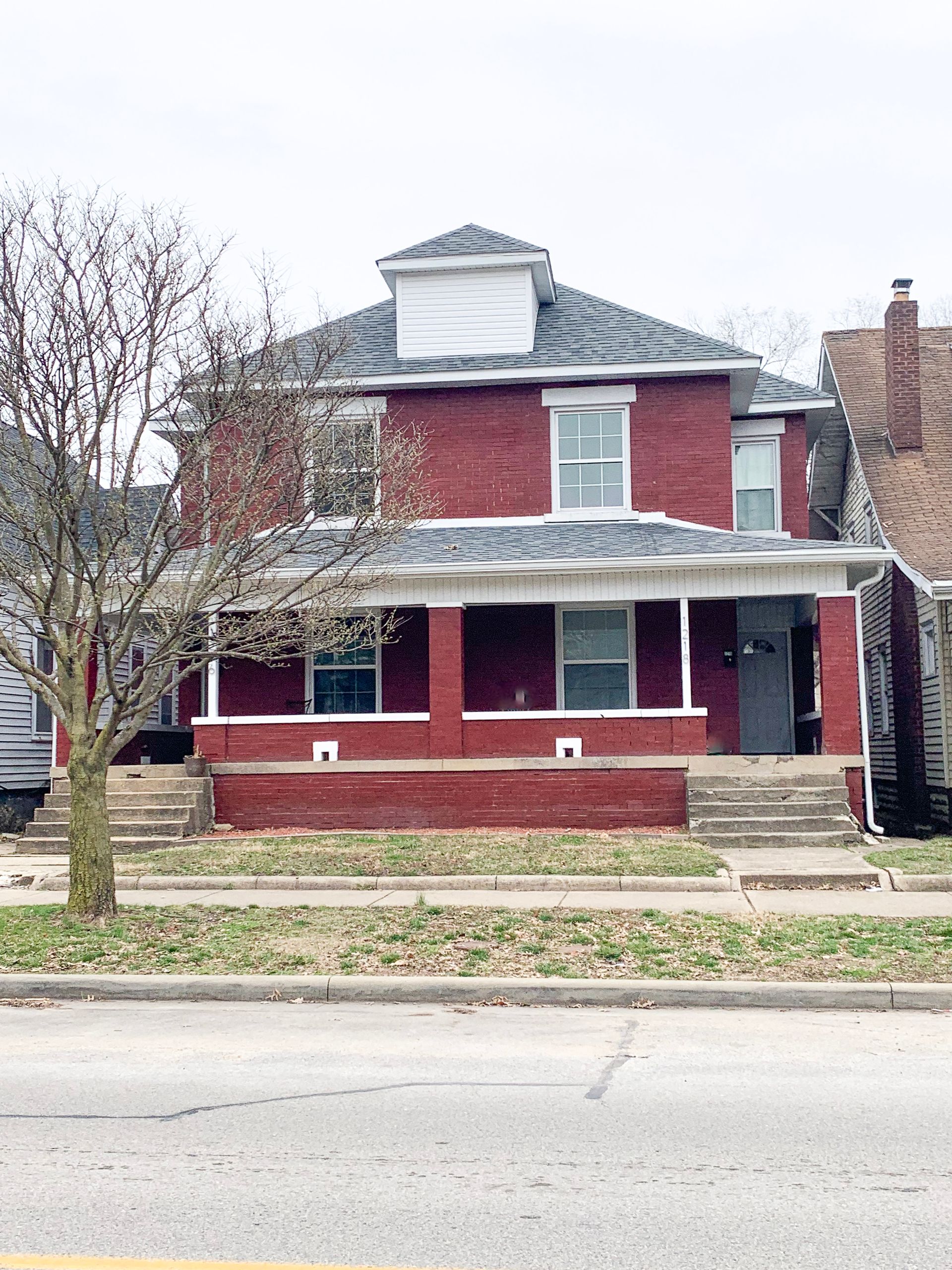 A red brick house with a gray roof is sitting on the corner of a street.