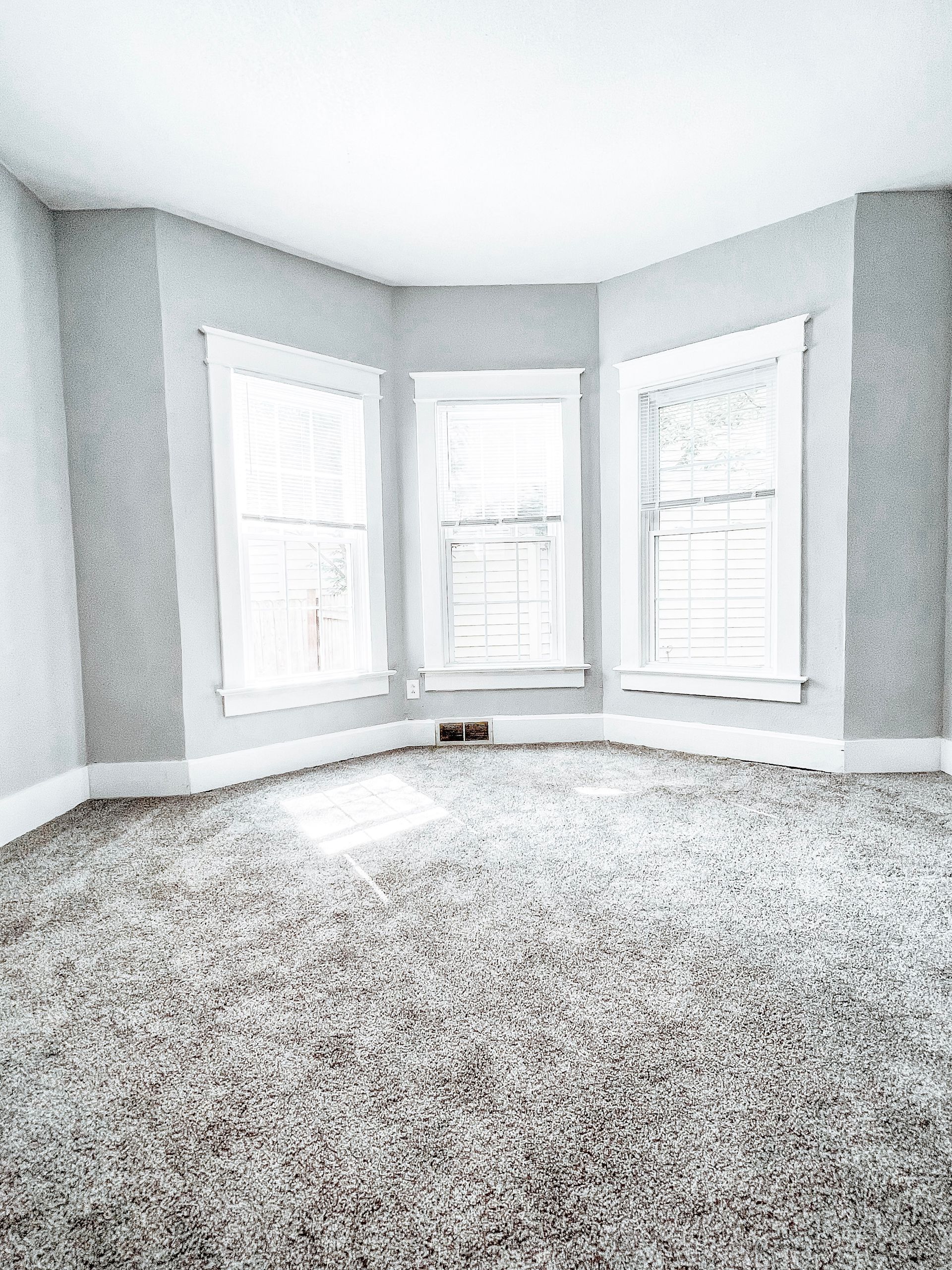 An empty room with a gray carpet and three windows.