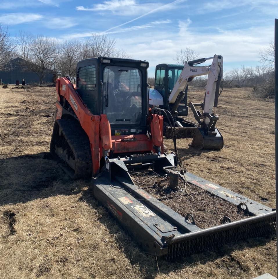 Red skid steer with mower attachment and a small excavator in a dry field under a blue sky