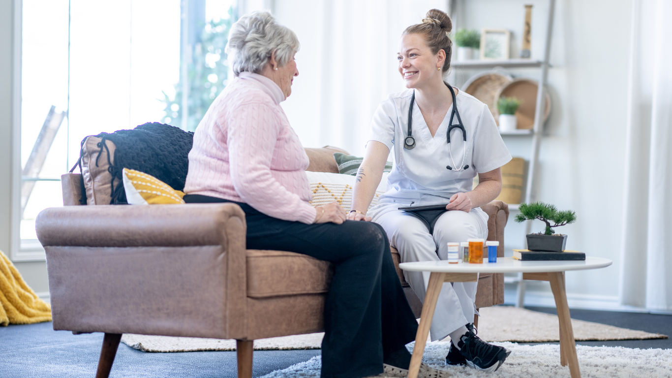 A healthcare worker checks an elderly woman's blood pressure in a living room.